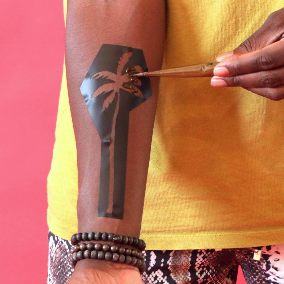 Palma - applying organic henna paste to a palm tree henna stencil on arm