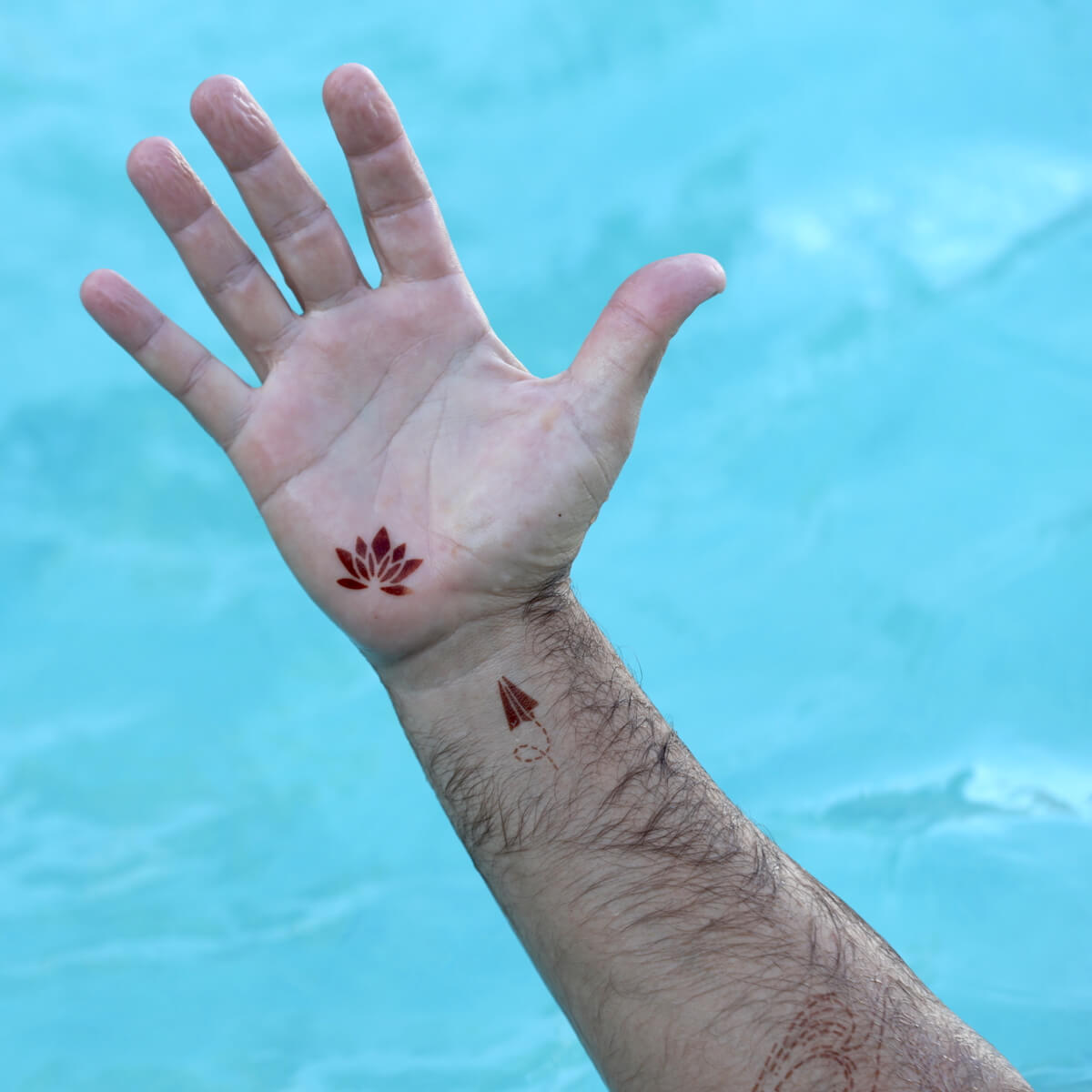 Sand - man wearing paper airplane and lotus mini henna tattoos on hand and wrist