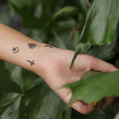 A woman’s hand adorned with jagua tattoo elements, including a crescent, cross, paw & diamond.