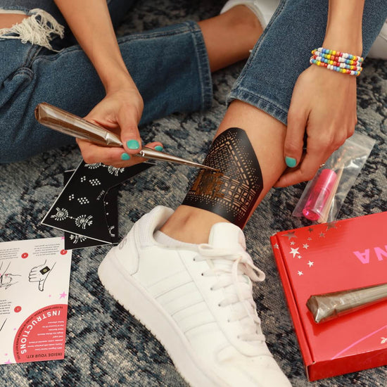 Woman uses henna cone to create a henna tattoo on her ankle