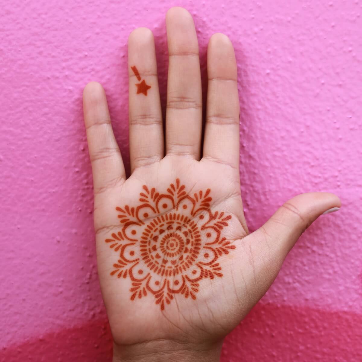 Mandala henna tattoo on palm against a pink wall
