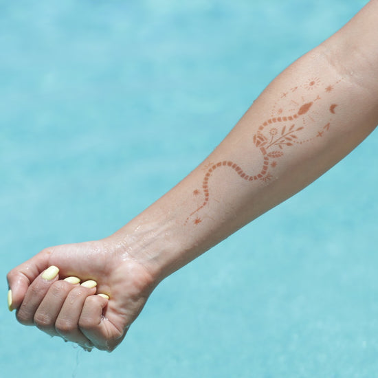 Sabrina - snake henna tattoo on forearm over blue water